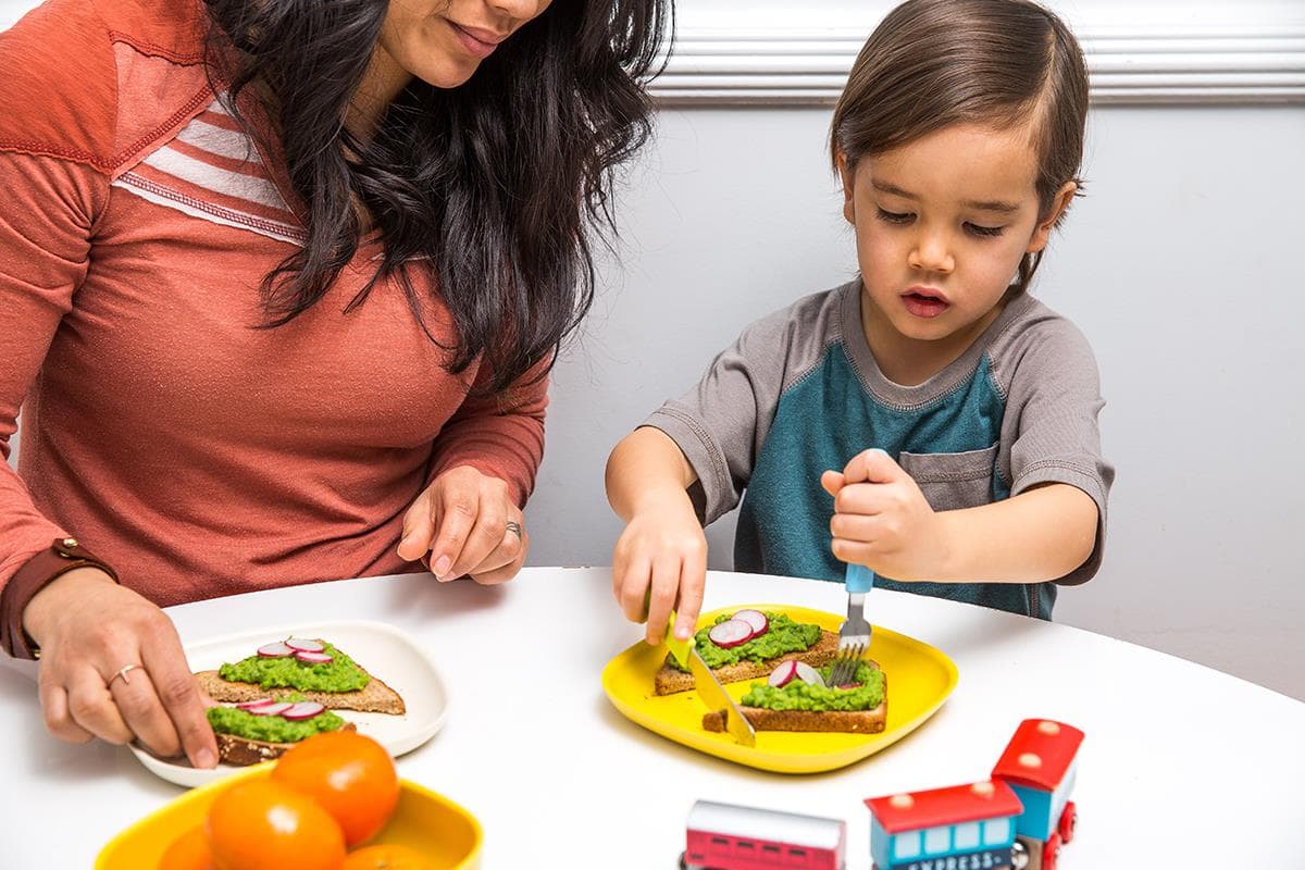 child and mom with cheesy pea toast at table